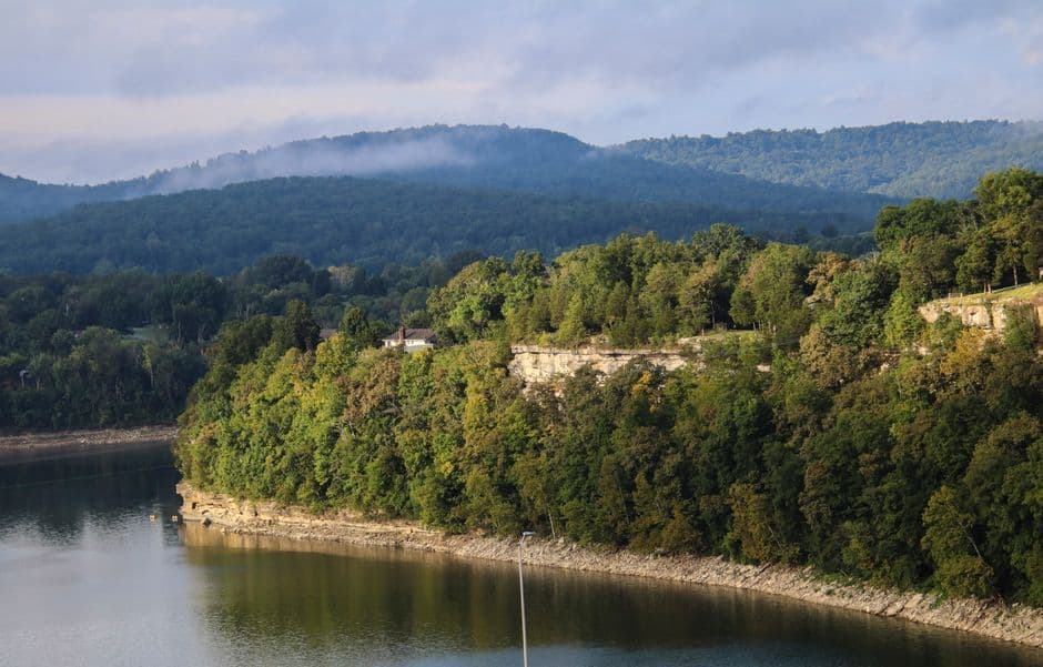 Peaceful landscape of the Ozarks with lush greenery by the water under a calm sky.